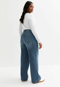 Högmidjade, vida jeans i medtvättad denim. Har fem fickor och ett subtilt sömnads mönster. Slät textur med avslappnad passform.