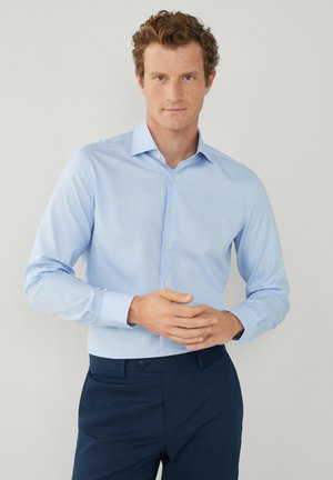 Lichtblauw, lange mouw dress shirt met een knoopsluiting aan de voorkant en een puntige kraag. Draagt met donkerblauwe broek, met een gladde textuur.