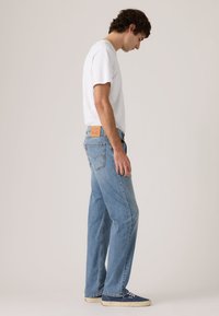 Ανοιχτό μπλε τζιν παντελόνι με ίσια γραμμή, ελαφρώς ξεθωριασμένη υφή και ταμπά δερμάτινο ταμπελάκι στο πίσω μέρος με λογότυπο. Συνδυάζεται με λευκό μπλουζάκι.