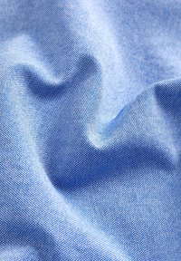 Mėlyna audinio medžiaga su mažomis, tolygiai išdėstytomis baltomis taškais. Tekstūra atrodo lygi ir šiek tiek atspindinti, su švelniais, plaukuojančiais raukšlėmis.