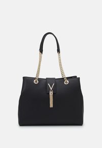 Svart handväska i texturerat material, med kedjehandtag i guld, en tofsdetalj och en frammagnetisk stängning med logotypdetalj.
