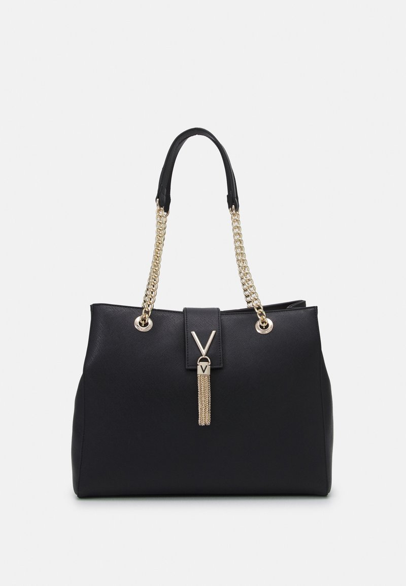 Black handbag made of textured material, featuring gold chain straps, a tassel accent, and a front magnetic closure with a logo detail.