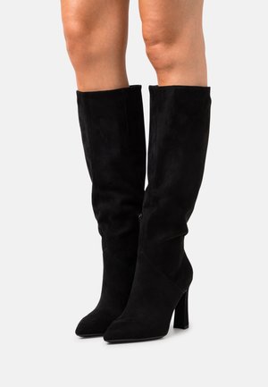 Bottes cuissardes en suède noir avec un bout pointu et un talon haut carré. Elles sont dotées d'une fermeture éclair latérale et d'une texture douce.