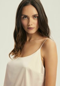 Jasnoróżowa satynowa koszulka na ramiączkach z cienkimi paskami, charakteryzująca się gładką teksturą i prostym wzornictwem. Zawiera dyskretny detal kieszeni z przodu.