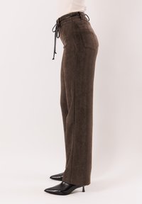 Pantaloni marroni a gamba larga in tessuto strutturato, con vita con coulisse e tasche posteriori, abbinati a tacchi neri a punta.