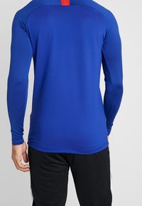 Pitkähihaiseen urheilupaitaan kirkkaan sininen väri, valmistettu sileästä ja kevyestä materiaalista. Paidassa on punainen yksityiskohta takana kaula-aukossa ja se on istuva malli.