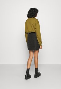 Felpa oversize verde oliva, mini gonna nera texturizzata con un motivo e stivaletti neri con suola spessa.