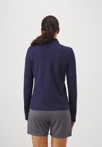 Haut à manches longues bleu marine avec un col haut, texture lisse et design ajusté ; associé à un short gris texturé, vu de dos.
