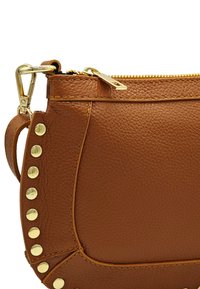 Sac à main en cuir marron avec une finition texturée, quincaillerie dorée, fermeture éclair sur le dessus et clous décoratifs dorés le long de la couture latérale.