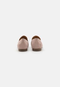 Mocassins en daim rose à finition lisse, avec un petit talon en bois marron et un discret logo à l'arrière, conçus pour un confort optimal.
