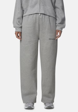 Personne portant un pantalon de jogging gris ample et des chaussures de sport grises, avec un sweat à capuche gris assorti partiellement visible.