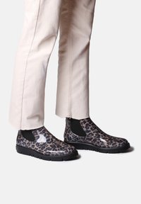 Bottines imprimé léopard avec des panneaux latéraux élastiques noirs et des semelles en caoutchouc texturées, associées à un pantalon croisé de couleur claire.