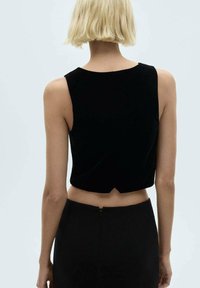 Černý sametový crop top s kulatým výstřihem a zapínáním na zádech, v kombinaci s černou sukní s vysokým pasem. Minimalistický design, hladká textura.