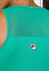 Žalia sportinė marškinėlių su atvira tinklo dalimi, lygiu audiniu ir maža logotipo etikete su raudonais, baltais ir juodais akcentais.