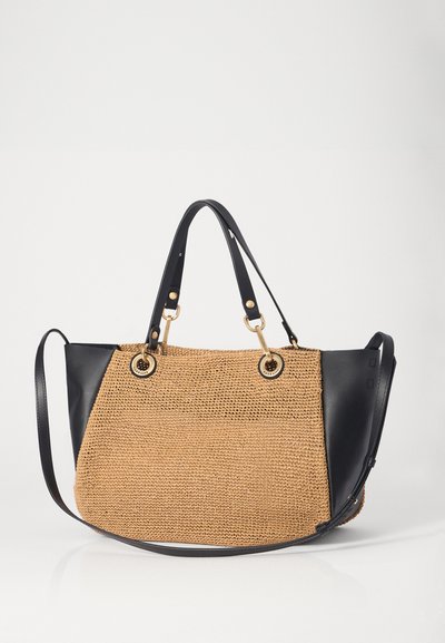 Woven tan straw handbag with black leather accents, featuring dual handles and gold hardware rings on the front. Adjustable shoulder strap included.