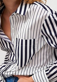 Button-up shirt with navy and white vertical stripes, featuring a chest pocket, a collar with contrasting stripes, and a relaxed fit.