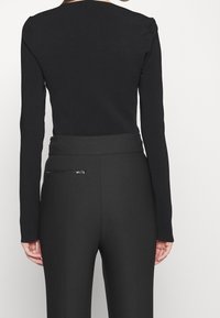 Svart långärmad topp kombinerad med svarta högmidjade byxor som har en elegant design och en liten dragkedjeficka på ena sidan.