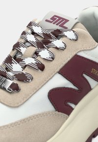Baskets avec une tige en daim beige, un panneau en maille blanche, des accents bordeaux et des lacets à motifs marron et blanc. Comprend une étiquette avec logo moulé.