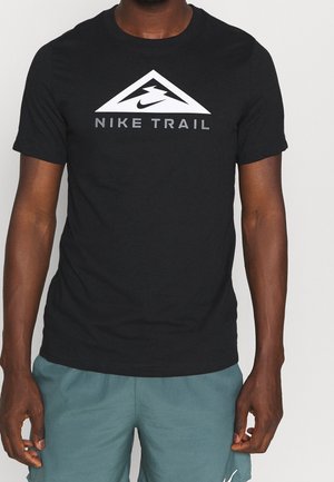 Mężczyzna noszący czarną koszulkę Nike Trail z białym logo góry i znakiem Swoosh, do tego turkusowe spodenki.