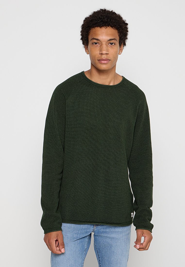 Donkergroene sweatshirt met een textuur breiwerk, ronde hals en lange mouwen, gecombineerd met lichtblauwe denim jeans.