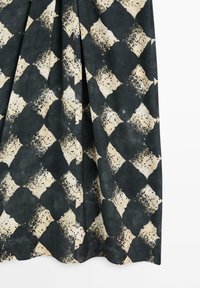 Dunkler Stoff mit einem geometrischen Muster aus unregelmäßigen beigen Diamantformen, die mit schwarzen Sprenkeln gesprenkelt sind, gezeigt in weichen Falten.