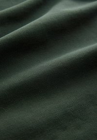 Dunkelgrüner Stoff mit strukturierten Oberflächen, der weich fallende Falten und eine glatte Oberfläche aufweist, geeignet für verschiedene textile Anwendungen.