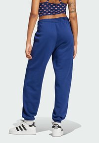 Blå mjukisbyxor med avslappnad passform, elastisk midja och mudd i anklarna, kombinerade med vita sneakers med svarta ränder.