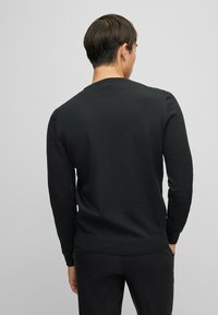 Schwarzer Strickpullover mit Rundhalsausschnitt, langen Ärmeln und fittedem Bund. Die Textur wirkt glatt mit einem dezenten Muster.