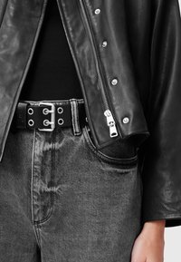 Zwarte leren jas met zilveren accenten, gecombineerd met een zwarte riem met metalen oogjes. Grijze spijkerbroek van denim met subtiele textuur en contrasterende stiksels.