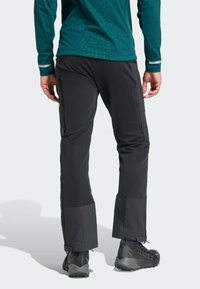 Pantalons noirs ajustés, dotés de zips latéraux et de poignets réglables. Fabriqués dans un matériau résistant et imperméable.