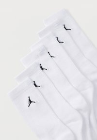 Seis pares de calcetines blancos de caña con el logo negro de Jumpman, apilados ordenadamente sobre un fondo blanco.