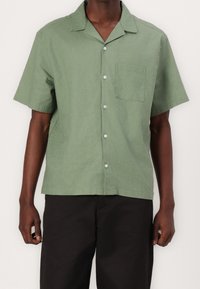 Camisa de botones de manga corta en verde, hecha de un tejido ligero; cuenta con un bolsillo en el pecho y un ajuste relajado con cuello.