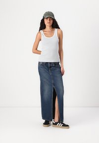 Canotta a righe bianche e blu abbinata a una gonna maxi di denim con uno spacco frontale. Sneakers nere con strisce bianche e un cappellino verde.