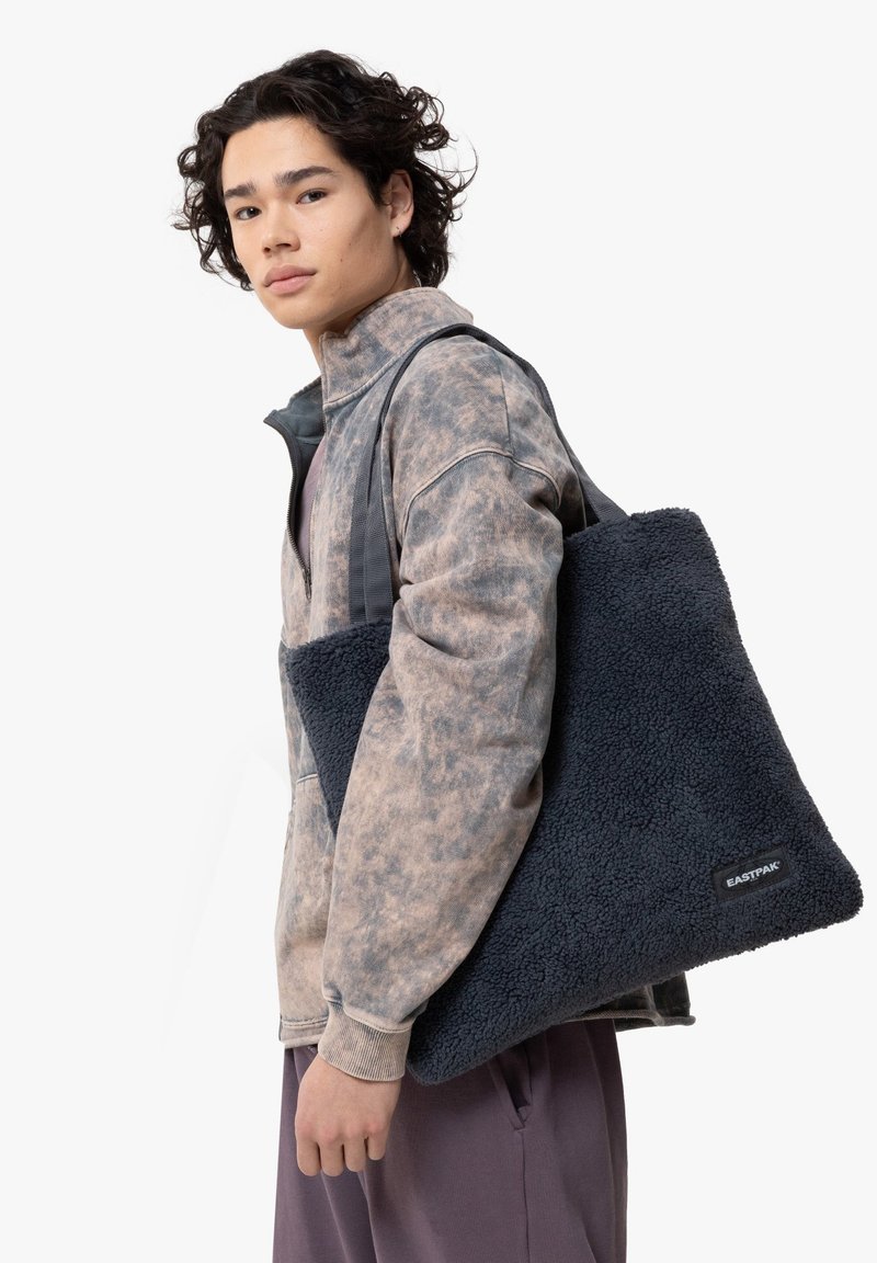 Borsa tote in pile blu con superficie testurizzata. Tessuto morbido, forma rettangolare e manici robusti. Presenta un'etichetta nera con il testo "EASTPAK".