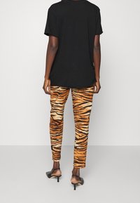 Zwarte oversize t-shirt, oranje en zwarte tijgergestreepte broek, gestructureerde stof, slim fit, gecombineerd met zwarte hakken.