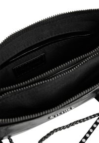 Interno della borsa in pelle nera con scomparto con zip, rivestimento in tessuto, tracolla a catena e piccolo dettaglio della tasca interna.