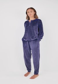 Velvet loungewear set in deep purple, featuring long sleeves and matching pants with scattered rhinestone accents. Soft, relaxed fit.