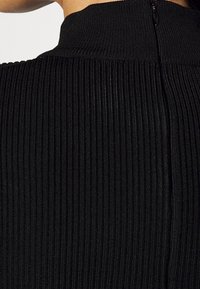 Zwart geribd stof met een hoog kraagontwerp en een verborgen rits aan de achterkant, die een gestructureerde en nauwsluitende vorm toont.