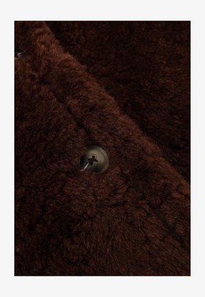 Bruine fleecestof met een zachte, gestructureerde oppervlakte en een opvallend knoopdetail dat rond en donker is, met vier gaten voor stikken.