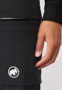 Zwarte geïsoleerde broek met een zijvak en een wit geborduurd olifantenlogo, een gladde textuur en subtiele reflecterende accenten.