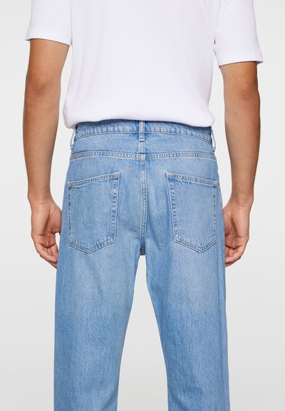 Ljust blå denimjeans med avslappnad passform, två bakfickor, synlig sömnad och midjeband, kombinerat med en enkel vit skjorta.