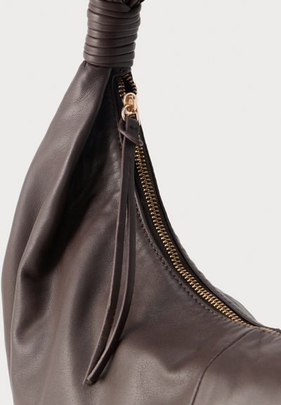Σκούρα καφέ δερμάτινη τσάντα με χρυστό φερμουάρ και μακριά δερμάτινη ταινία φερμουάρ, που διαθέτει λεπτομέρεια με χοντρό, τυλιγμένο λουρί στο επάνω μέρος.