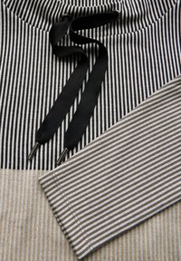 Gestreepte stofdetail met zwarte, witte en beige secties, met een zwarte trekkoorden en zilveren hardwareaccenten.