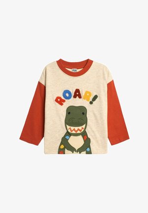 Krémovo-červená košeľa s dlhým rukávom, na ktorej je grafika zeleného dinosaura a nápis "ROAR!" v farebných písmenách. Obsahuje textúrované vyšívané detaily.