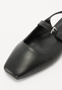 Pantof cu toc pătrat din piele neagră, cu un design decupat și o curea îngustă prinsa cu o cataramă argintie. Textură netedă cu accente minime.