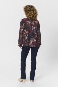 Blusa a fiori con maniche lunghe, fondo scuro e tonalità di rosso, rosa e crema. Abbinata a jeans scuri e tacchi di colore chiaro.
