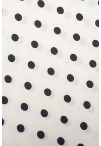 Witte stof met gelijkmatig verdeelde zwarte stippen in diagonale rijen, wat een klassiek patroonontwerp creëert.