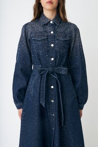 Τζιν φόρεμα σε σκούρο μπλε με διακοσμητικά με καρφιά, μπροστινό μέρος με κουμπιά, δύο τσέπες στο στήθος, μανίκια με μανσέτες και ζώνη από το ίδιο ύφασμα.