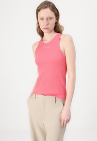 Tettsittende rosa ribbestrikket tanktop med rund hals og "PINKO"-logo, kombinert med lyse beige bukser. Glatt tekstur og ermeløs design.