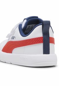 Sneaker blanc avec des accents rouges et navy, présentant une tige en cuir lisse, un col rembourré et une semelle en caoutchouc avec une adhérence texturée.